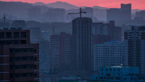 黃昏的城市景觀，高樓和起重機在粉紅色天空的背景下。