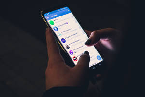 特寫雙手在夜間拿著顯示Telegram應用程式的智能手機。