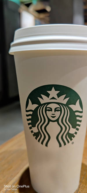 白色Starbucks咖啡杯，帶有綠色標誌，置於木桌上。 — Pixel 9 壁紙