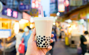 喺繁忙嘅夜市中，手拎住泡泡茶，旁邊有發光嘅招牌。