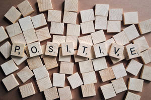 在棕色背景上拼出「positive」的 Scrabble 字母磚 — 勵志桌面 壁紙