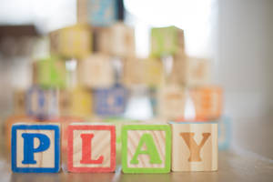 木製積木拼出play，背景有模糊的字母積木。