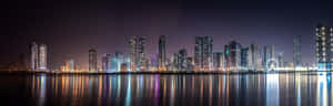 夜晚的城市景觀，發光的摩天大樓倒映在水中。 — 天際線 壁紙