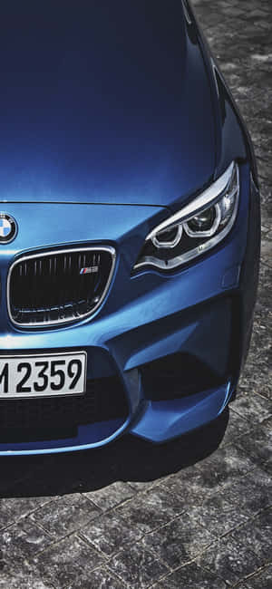 藍色BMW M2跑車前視圖，在鵝卵石路面上。 — iPhone 17 壁紙