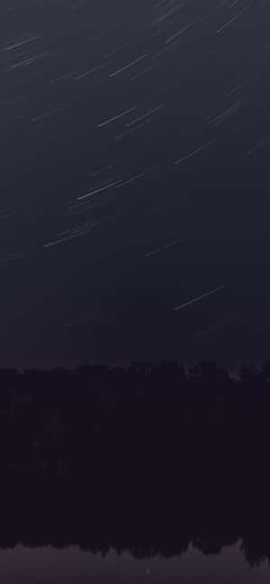 夜晚，星軌在平靜水面上倒映的黑暗森林上方。