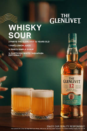 兩杯威士忌酸飲料和一瓶 Glenlivet 12 年威士忌放在木製吧檯上，有手伸進來。