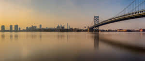 日落時的班傑明·富蘭克林大橋，城市天際線倒映在平靜的水面上。 — 日落大道 壁紙