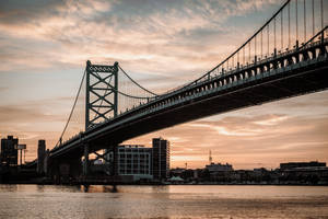 金色夕陽下，水上的吊橋，背景是城市天際線。