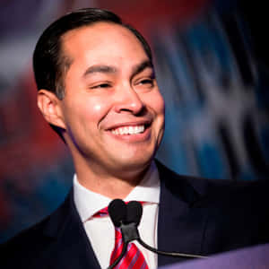 身穿西裝和紅色領帶的男子在演講時對著麥克風微笑。 — 政治 壁紙