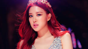 K-pop表演者，紅髮戴頭飾，身穿閃亮服裝，在舞台燈光下。