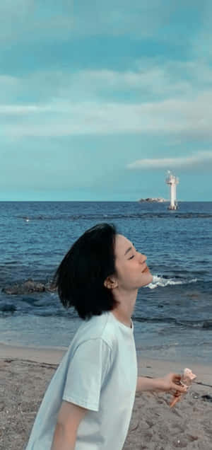年輕女子在海灘上享用冰淇淋，遠處有燈塔。