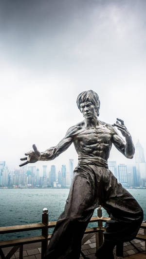 李小龍武術姿勢的青銅雕像，位於碼頭，背景為城市天際線。