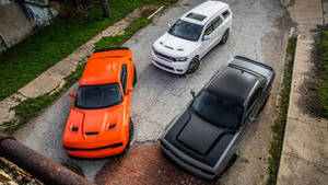 三輛Dodge Challengers停泊在一條有草叢邊緣的裂縫街道上。 — 汽車 壁紙