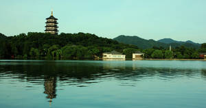 寶塔倒映在平靜的湖面上，四周環繞著翠綠的山丘和傳統建築。 — 唐人街 GIF 壁紙