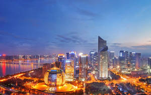 黃昏時分的現代城市天際線，燈火通明的建築物和河流倒影。 — 唐人街 GIF 壁紙