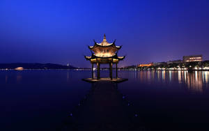 夜間湖上碼頭上的亮燈亭子，城市燈光倒映在水中。 — 湖景 壁紙
