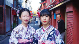 兩位年輕女性穿著色彩繽紛的和服，在狹窄的日本小巷中擺姿勢。