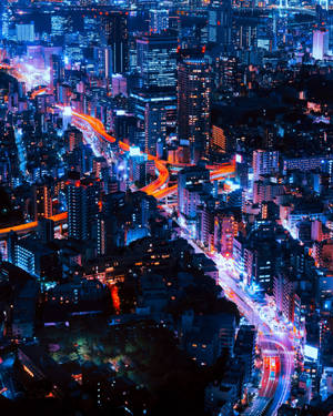 充滿活力的城市夜景鳥瞰圖，有發光的藍色建築物和交通的橙色光跡。 — 日本 壁紙