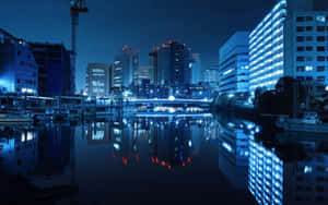 夜晚城市天際線倒映在平靜的河流中，有發光的建築物和橋樑。 — 日本 壁紙