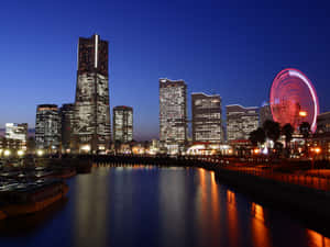 夜間城市景觀，燈火通明的建築物和摩天輪倒映在水中。 — 夜景城市 壁紙