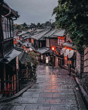 濕滑的石階沿著一條狹窄的日本街道向上延伸，兩旁是傳統木建築，被溫暖的燈籠照亮。
