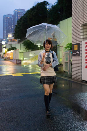 日本女學生在黃昏的城市街道上撐著透明雨傘在雨中行走。