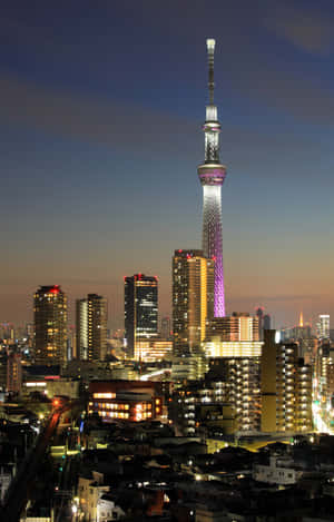 東京晴空塔在黃昏的城市景觀中閃耀著紫色和白色的光芒。 — Honor Pad X8b 壁紙