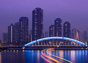 夜晚水上藍色燈光橋樑，帶有汽車燈光軌跡和城市建築。