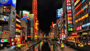 夜晚的東京運河，兩旁是發光的霓虹燈招牌和建築物。 — 東京卍復仇者 壁紙