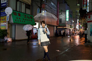 一名日本女學生在夜晚的雨街中撐著透明雨傘行走。