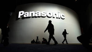 在黑暗的房間中，人們的剪影走過一個大型發光的Panasonic標誌。