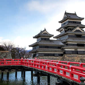 紅色橋樑通往傳統日本城堡，擁有分層屋頂和石牆。 — 日本 壁紙