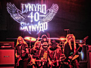 Lynyrd Skynyrd 樂隊在舞台上現場表演，身後有發光的翅膀標誌。