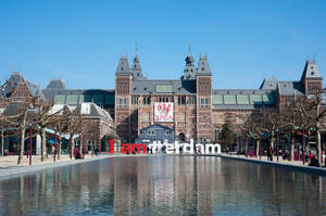 阿姆斯特丹國立博物館與「I am Amsterdam」標誌在陽光下倒映在水中。 — 建築 壁紙