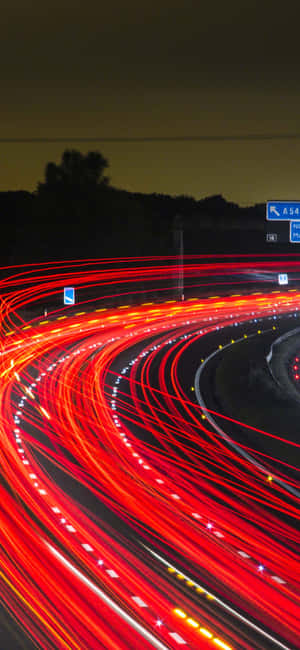 夜間高速公路，紅色汽車燈光在黑暗中蜿蜒形成條紋。 — iPhone 16 Plus 壁紙