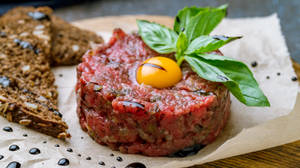 高級牛肉他他配鵪鶉蛋和羅勒，放在牛油紙上，附有麵包。