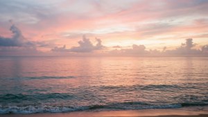 海浪輕輕拍打沙灘，粉橙色夕陽天空下散佈著雲朵