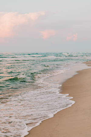 海洋波浪在日落時輕輕沖刷沙灘，天空呈現粉彩色。 — 沙灘 壁紙