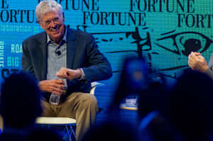 一位長者在Fortune活動中發言時微笑，前景有觀眾。