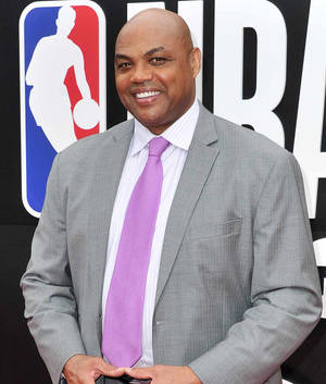 一位身穿灰色西裝和紫色領帶的男士在NBA活動中微笑。