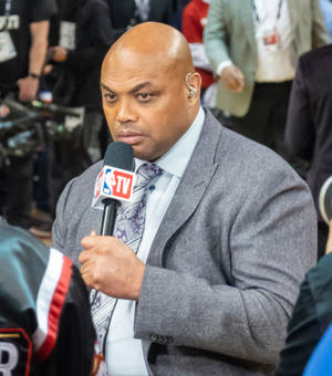 NBA TV體育記者穿著灰色西裝，在直播中手持麥克風。