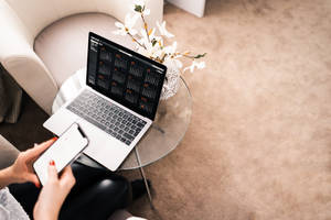 Person using laptop and phone on glass table in modern living room.