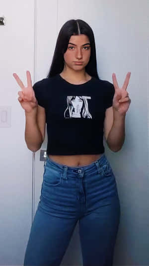年輕女性身穿黑色露臍上衣和牛仔褲在室內比出和平手勢。