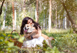 女性在陽光明媚的森林中擁抱哥基犬，旁邊有野餐籃。