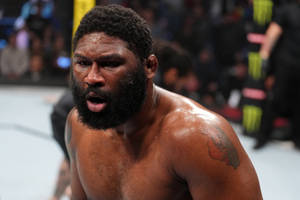 一個肌肉發達、留鬍子的MMA拳手在八角籠比賽中表情痛苦。