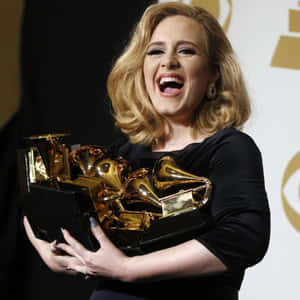 Adele 在舞台上捧著多個格林美獎座大笑。