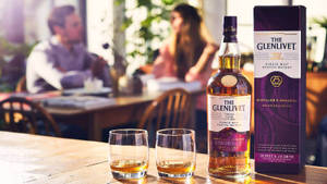 餐廳木桌上的一瓶Glenlivet威士忌和兩個酒杯。