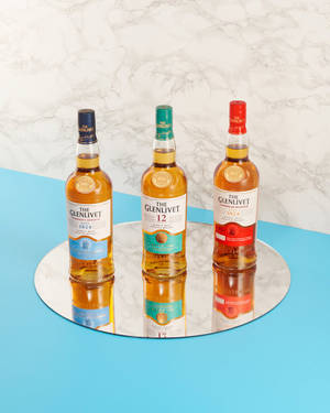 三瓶Glenlivet威士忌酒瓶排列在帶有大理石和藍色背景的鏡面托盤上。