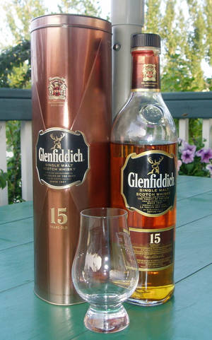Glenfiddich 15年威士忌瓶和杯子放在戶外的綠色桌子上。