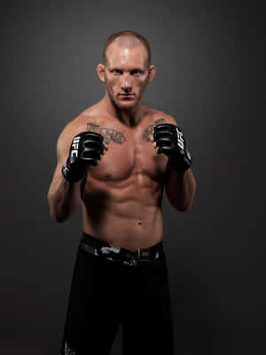 一名赤裸上身的男性拳手，戴著黑色UFC手套和穿著黑色短褲，擺出戰鬥姿勢。 — 戰士 壁紙